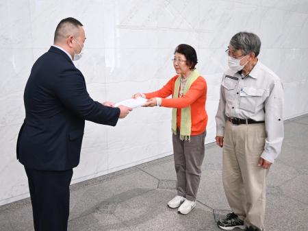 　北陸電力本店を訪れ、担当者（左）に議案を手渡す市民団体のメンバーら＝２５日午後、富山市