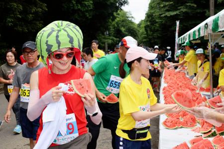 　千葉県富里市で開かれたマラソン大会「富里スイカロードレース」で、スイカを手に取るランナーたち＝１６日午前