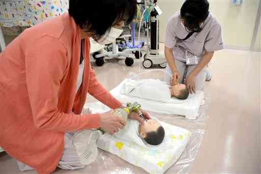 酸素バッグを使って赤ちゃんに酸素を吸入する場面を再現する看護師（手前）。奥は酸素ボンベから赤ちゃんに酸素を与える場面＝熊本市民病院