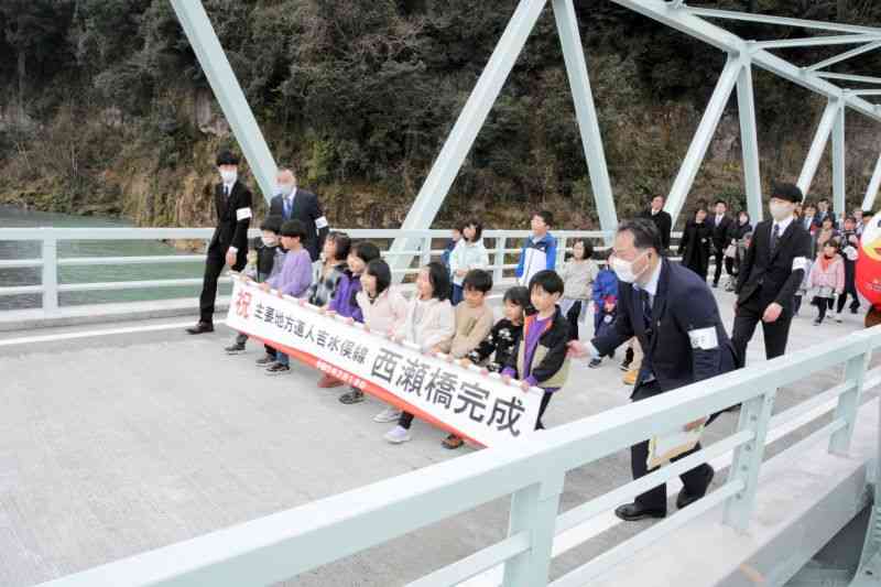球磨川の西瀬橋が復旧し、横断幕を手に歩いて渡る児童ら＝人吉市