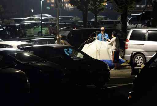 車中泊の車の間にテントを張る避難者。厳しい避難生活で健康への悪影響も懸念される＝４月２９日、益城町のグランメッセ熊本（大倉尚隆）