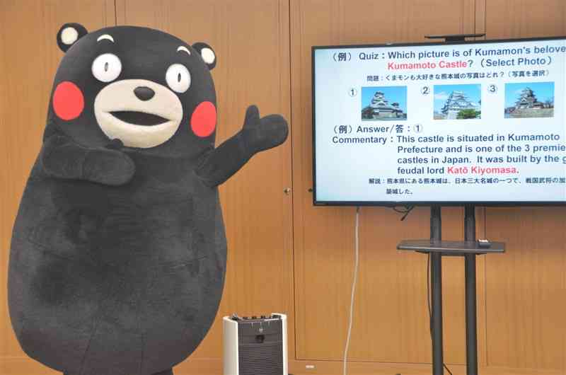 英語など3言語を用いた「くまモンクイズ」で、熊本城の写真を選ぶ問題を紹介するくまモン＝28日、県庁