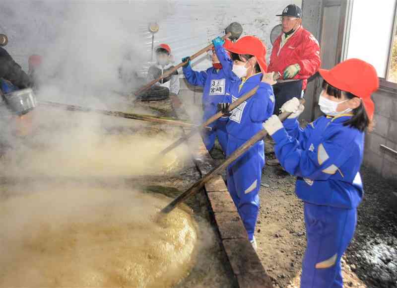 サトウキビの煮汁を大きな釜で煮つめる青海小の児童＝3日、宇城市