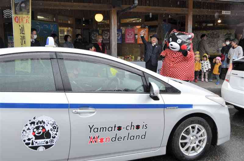 くまモンがラッピングされたタクシーの出発を祝う観光関係者ら＝28日、山都町