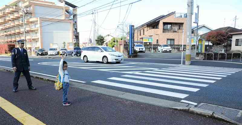信号機のない横断歩道を渡る前に、手を上げてドライバーに知らせる子ども。辺りが薄暗くても目立つよう、明るめの服装がおすすめ＝3月下旬、熊本市中央区