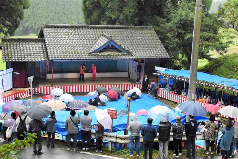 美里町の勢井阿蘇神社の農村舞台で開かれた願成祭。左に花道、右に桟敷席が見える。小雨が降り傘の花が咲く中、地区民らの笑い声や歓声が鎮守の森に響いていた