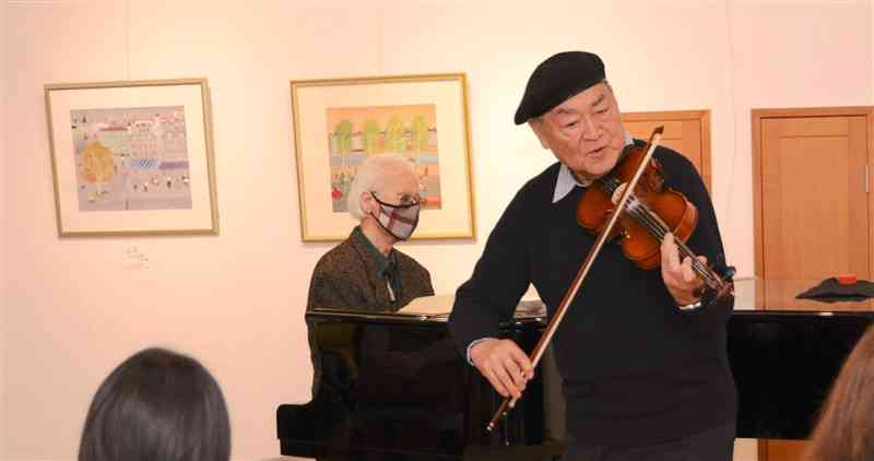 自らの絵画作品の前でジャズを演奏するサン村田さん（右）＝2023年1月、人吉市