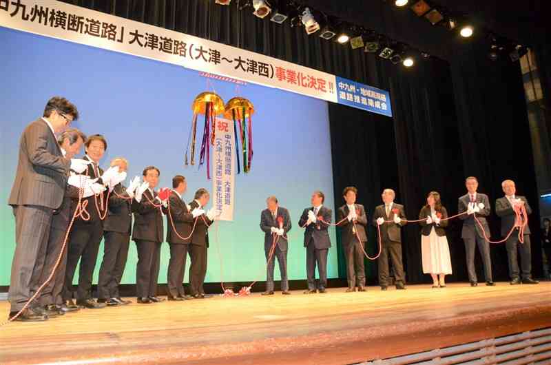 大津道路の事業化を祝い、関係首長や県議らが登壇し、くす玉を割った＝24日、大津町