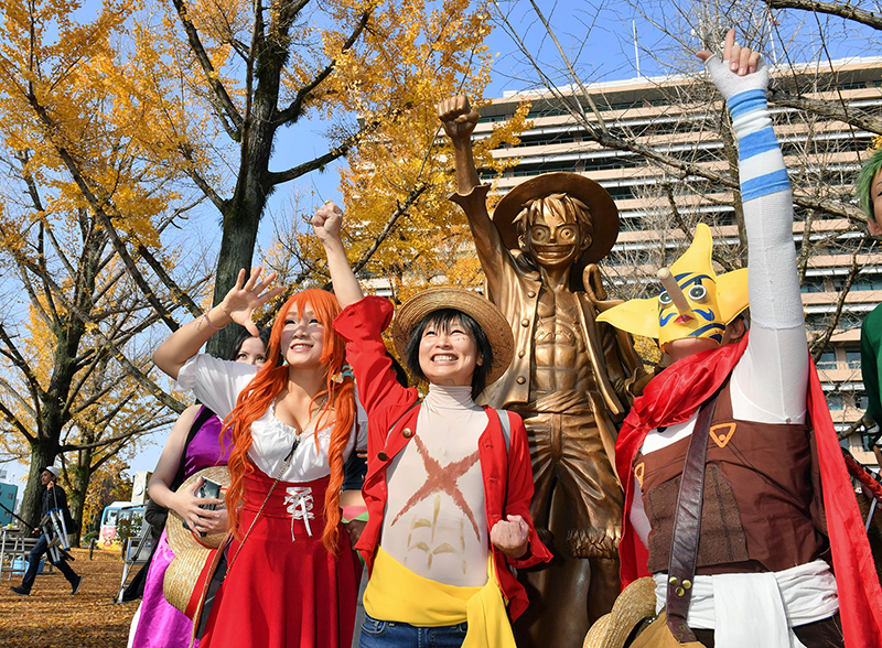 県庁プロムナードに設置された漫画「ワンピース」の主人公ルフィのブロンズ像と一緒に記念撮影する仮装した人たち＝2018年11月30日午後、熊本市中央区