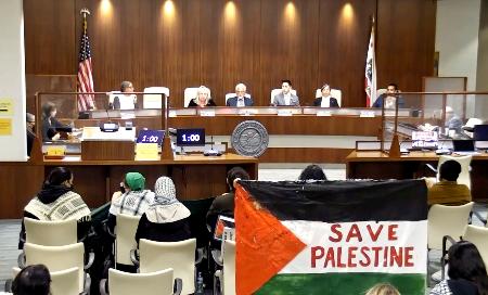 　２４日、米リッチモンド市で開かれた公聴会。傍聴者が掲げるパレスチナの旗に「パレスチナを救え」と書かれている（同市提供、共同）