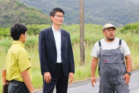 　水田の視察に訪れた朝日健太郎環境政務官（中央）に説明する「奄美稲作保存会」代表の小池弘章さん（右）＝１１日、鹿児島県龍郷町