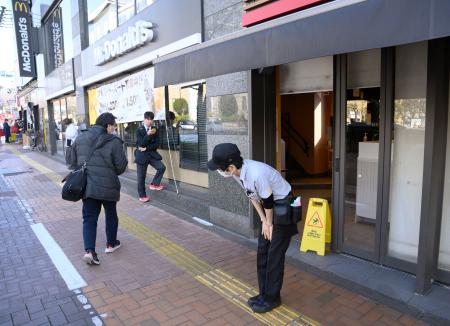 　モバイルオーダーや対面での注文が受けられない状態が続き、店舗の前で頭を下げるマクドナルドの店員＝１５日午後３時１１分、東京都内