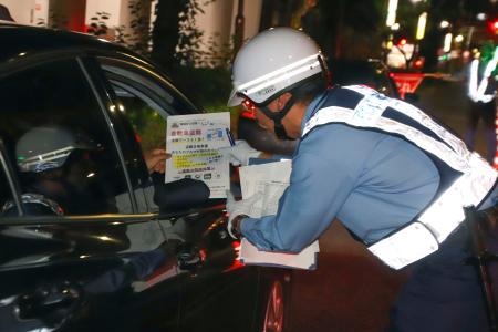 　ドライバーにビラを手渡す警察官＝２２日午前３時半、名古屋市