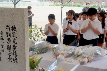 　米軍機墜落事故の犠牲者の名前が刻まれた「仲よし地蔵」に手を合わせる子どもたち＝３０日午前、沖縄県うるま市の宮森小