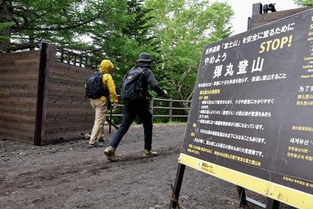 　富士山の山開きを前に、山梨県側から登山に向かう人たち。手前は「弾丸登山」への注意を呼びかける看板＝３０日午前
