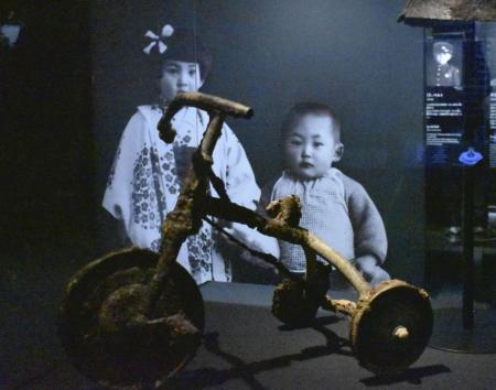 　原爆資料館に展示されている、鉄谷伸一ちゃん（写真右）の遺品の三輪車＝広島市