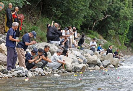 　２０２０年７月豪雨の犠牲者を悼み、球磨川支流の川内川に花を流し、手を合わせる住民ら＝４日午後、熊本県球磨村
