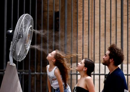 　イタリア・ローマの円形闘技場遺跡コロッセオ周辺に設置された扇風機の前に立つ人たち＝６月２１日（ロイター＝共同）
