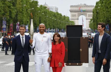 　パリ五輪の聖火リレーがパリ市内で始まり、シャンゼリゼ通りでトーチを手にするサッカーの元フランス代表ティエリ・アンリさん（左から２人目）ら＝１４日（共同）