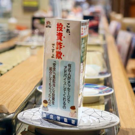 　小皿にのってレーンを流れる、投資詐欺被害防止を呼びかけるカード＝奈良市の大起水産回転寿司奈良店