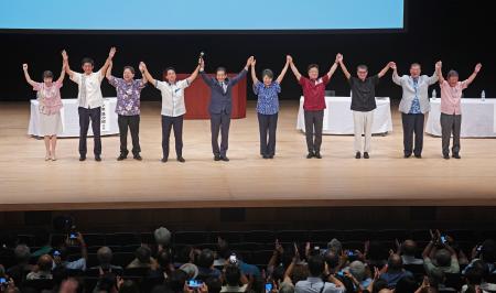 　自民党総裁選の演説会で、手を取り合う（左から）高市経済安保相、小林前経済安保相、林官房長官、小泉元環境相、（１人おいて）上川外相、加藤元官房長官、河野デジタル相、石破元幹事長、茂木幹事長＝１７日午後、那覇市