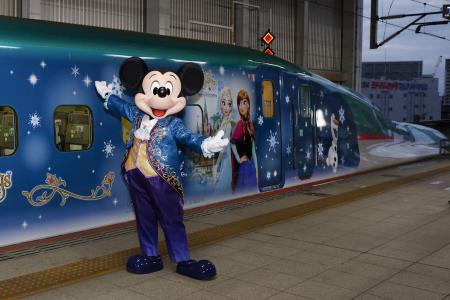 　ディズニーのキャラクターが車両にラッピングされた新幹線の前でポーズをとるミッキーマウス＝１０日午前、ＪＲ仙台駅