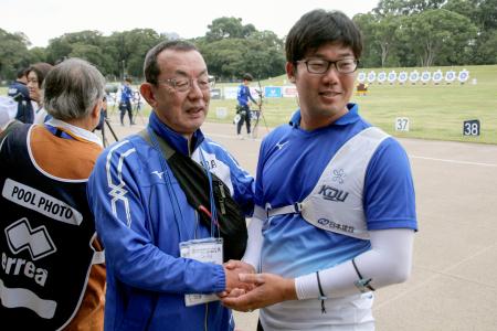 　現役最後の試合を終え、近大の山田秀明監督（左）と握手するアーチェリー男子の古川高晴＝夢の島公園アーチェリー場