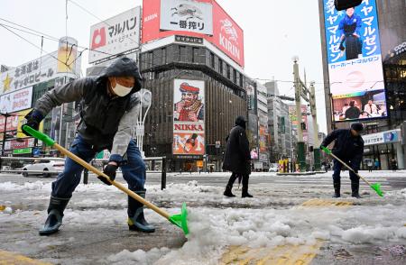 　札幌市の繁華街・ススキノで雪かきをする人たち＝７日午前