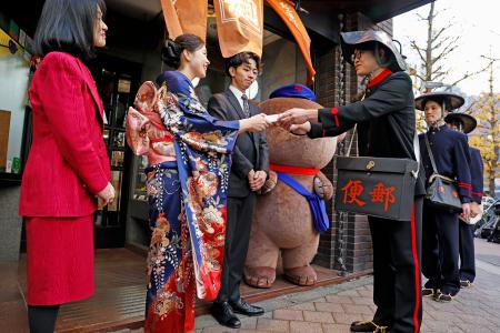 　明治時代の制服で年賀状を手渡す配達員（右）＝１日朝、東京都新宿区