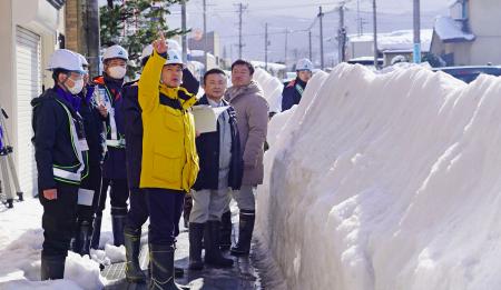 　除排雪が滞る青森県弘前市を視察する宮下宗一郎知事（中央）。県道の両脇に雪の壁ができている＝７日午前