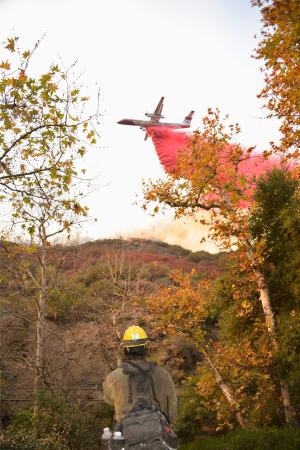 　延焼防止剤を投下する飛行機と無線連絡を取る消防隊員＝１１日、米ロサンゼルス（共同）