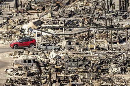 　火事で焼失した建物脇を走行する乗用車＝１２日、米ロサンゼルス（ＡＰ＝共同）