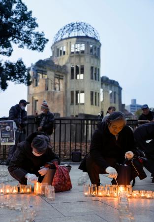 　核兵器禁止条約の発効から４年となり、広島市の原爆ドーム前でキャンドルに火をともす参加者ら＝２２日午後