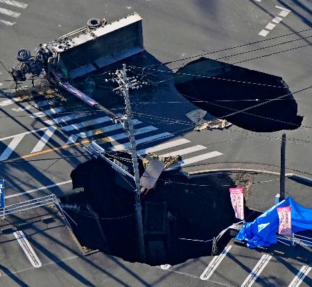 　道路が陥没しトラックが転落した穴（上）と引き上げられた荷台部分。手前は未明の作業中に新たに発生した陥没＝２９日午前８時２３分、埼玉県八潮市（共同通信社ヘリから）