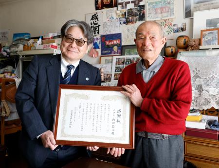 　仙台大分県人会会長の原田善教・東北学院理事長（左）から感謝状を受け取り、笑顔の内田菊治さん＝１３日午後、仙台市