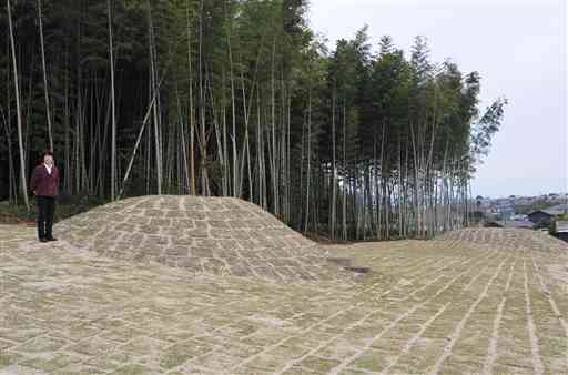 芝生を植えて整備した古墳２基の横に立つ新永惠美さん＝熊本市北区