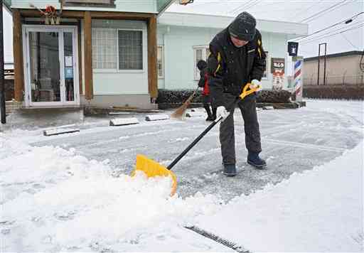 店の駐車場に積もった雪を取り除く人たち＝７日午前７時４０分ごろ、阿蘇市一の宮町（山下友吾）