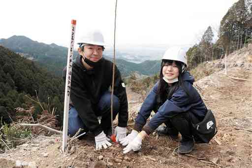 国有林の斜面にサクラの苗木を植える緒良中隆人さん、千夏子さん夫妻＝山鹿市