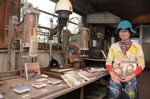 「トーフギャラリー」を開設した岡松トモキさん。豆腐をつくる機材の間に写真を展示している＝荒尾市