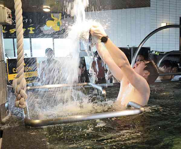 「ととのいタオル」に、滝のように流れ落ちる冷水を浴びせる参加者＝熊本市中央区