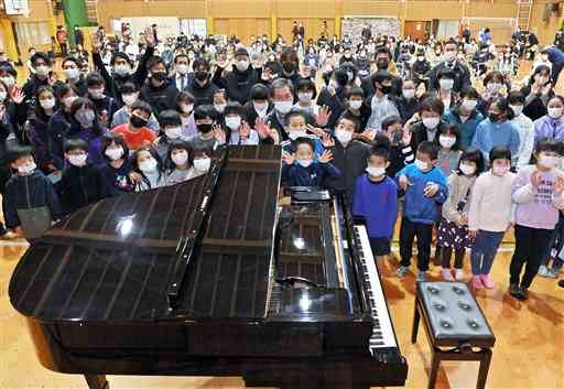 修復されたグランドピアノと一緒に記念写真に納まる渡小の児童ら。中央の男性が福島県いわき市の調律師遠藤洋さん＝２１日午後、球磨村の一勝地小（高見伸）