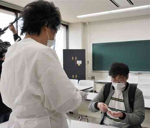 ＰＣＲ検査で検体を採取する熊本学園大の学生（右）＝２２日、熊本市中央区