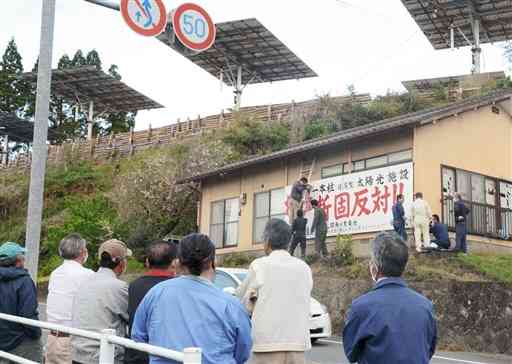 太陽追尾型発電施設（写真上）の撤去を求め、大型看板を設置する住民たち＝菊池市