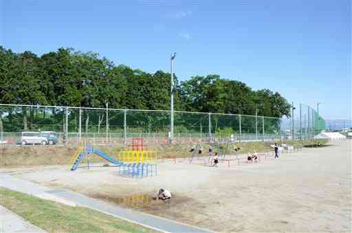 合志楓の森小・中学校の運動場で遊ぶ子どもたち。同校から、国立ハンセン病療養所・菊池恵楓園の樹木が見える＝合志市