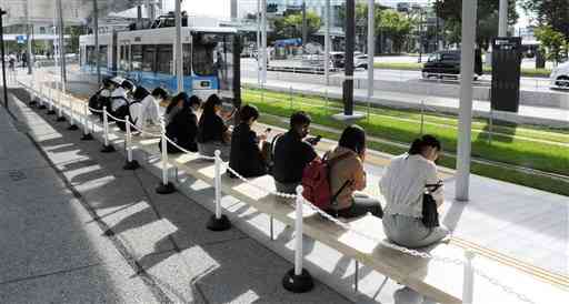 市電熊本駅前電停のベンチに座って電車を待つ乗客＝17日、熊本市西区