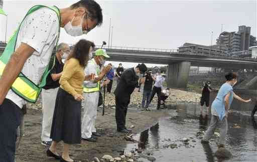 白川に向かって手を合わせ、犠牲者を悼む参列者。奥は子飼橋＝２６日、熊本市中央区