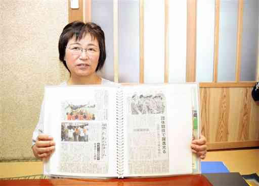 北里謙治の高校時代の新聞記事を切り抜いたスクラップ帳を手にする母の昭子さん＝小国町