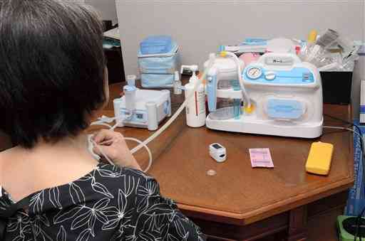 コロナに感染後、後遺症に悩む女性。気管切開した部分から１日３回程度、機器を使ってたんを吸引している＝熊本市