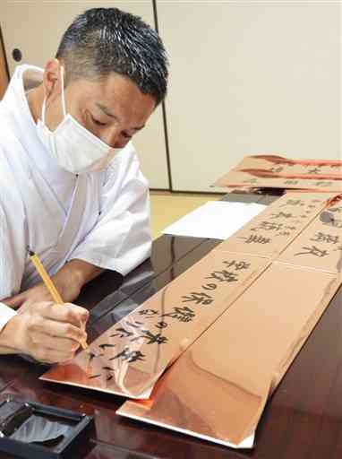 子どもたちの夢を銅板に代筆する木山神宮の禰宜の矢田幸貴さん＝益城町