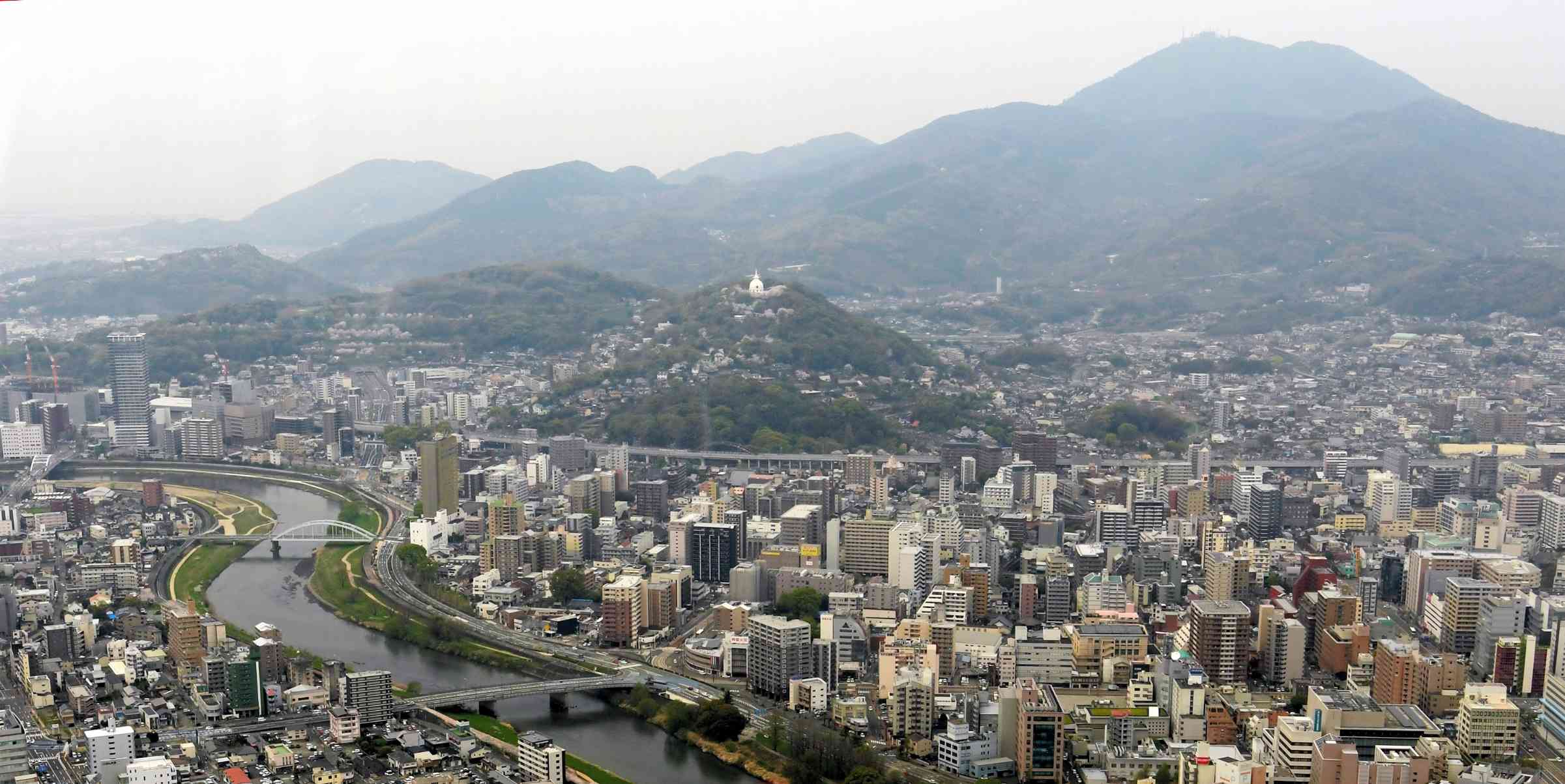 上空から見た花岡山（中央の仏舎利塔がある山）と万日山（花岡山の左横）。左奧に独鈷山、右上は金峰山＝４月３日、熊本市（小野宏明）